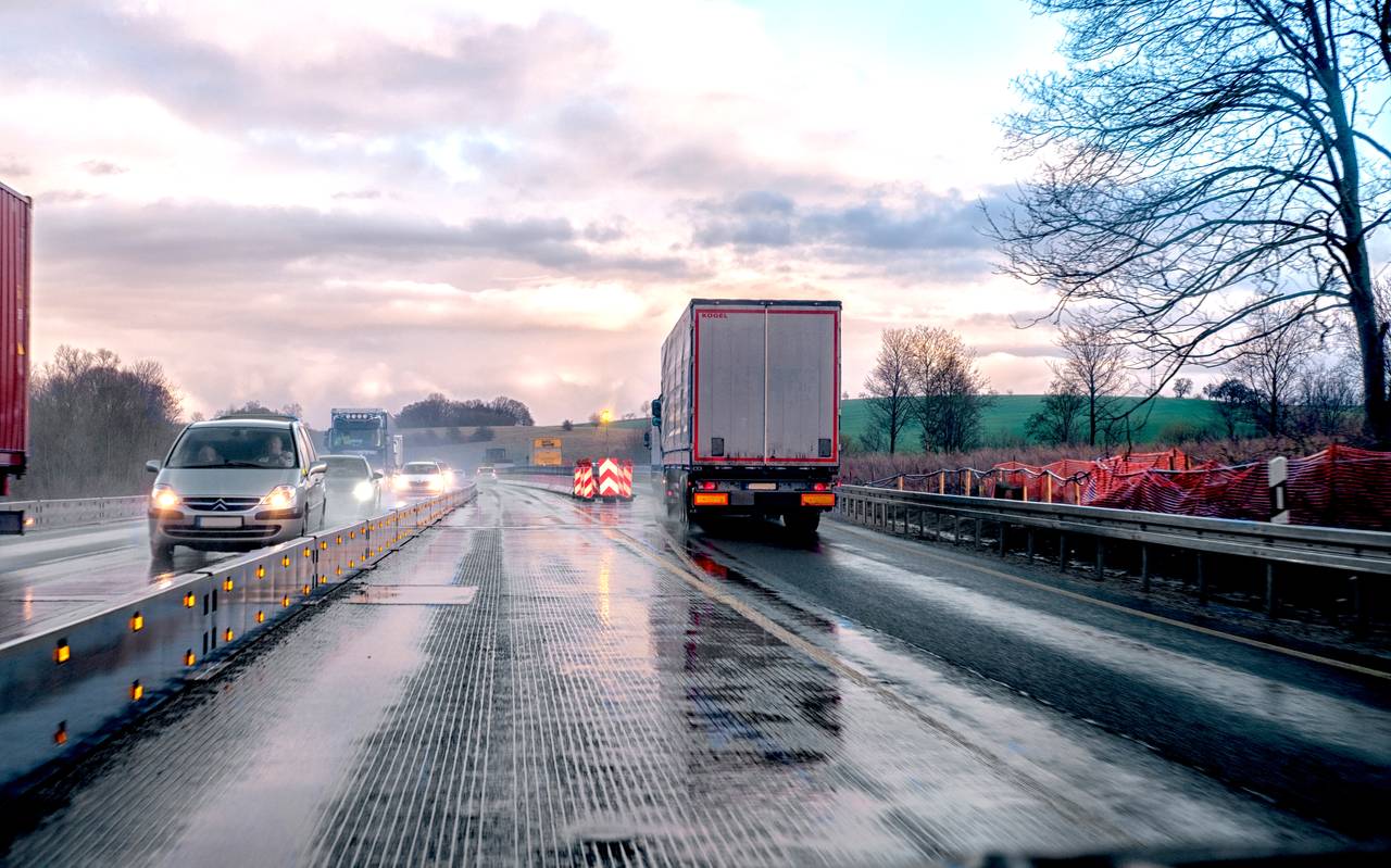 Eine verengte Fahrspur auf einer deutschen Autobahn, die ein nass-kaltes Wetter zeigt, bei dem im Gegenverkehr die Scheinwerfer der Autos erkennbar sind.