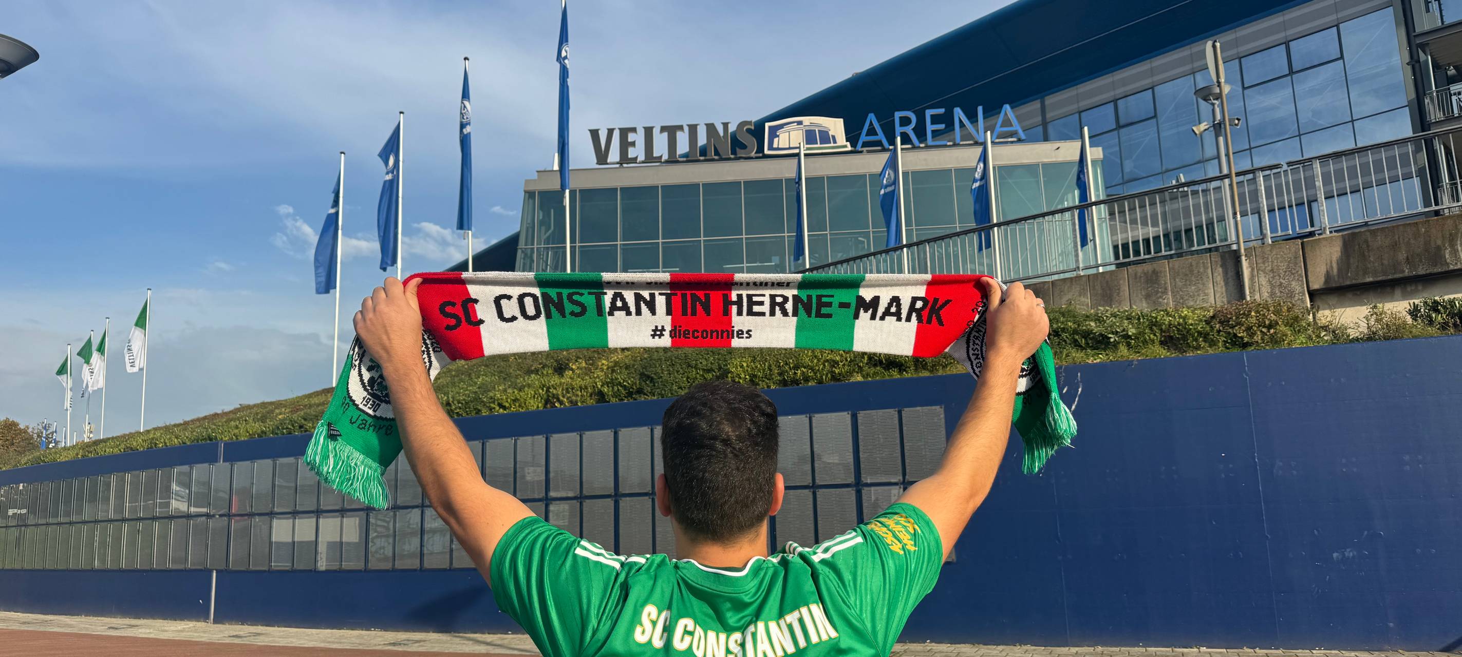 Ein Fußballfan steht vor der Arena auf Schalke und hält einen Fanschal des SC Constantin in die Luft. | Foto: Chris Störbeck / SC Constantin