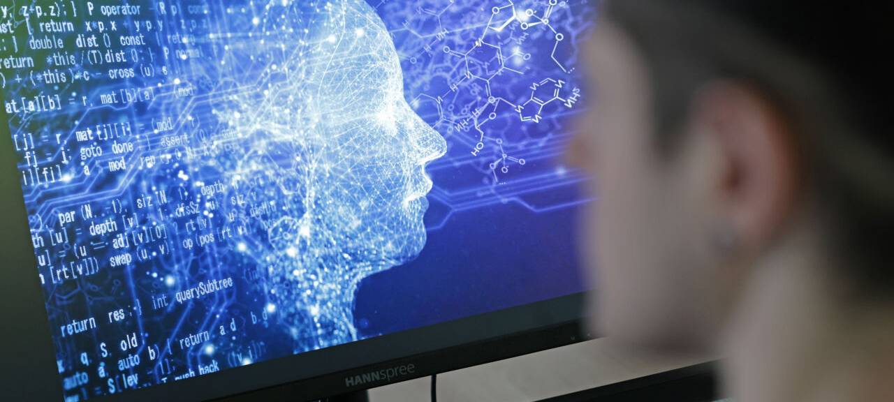 Eine Person sitzt vor einem Bildschirm, auf dem zu erkennen ist, dass es neben dem menschlichen Kopf auch verschiedene Ströme gibt, die fließen. Eine Art Symbolbild für Künstliche Intelligenz