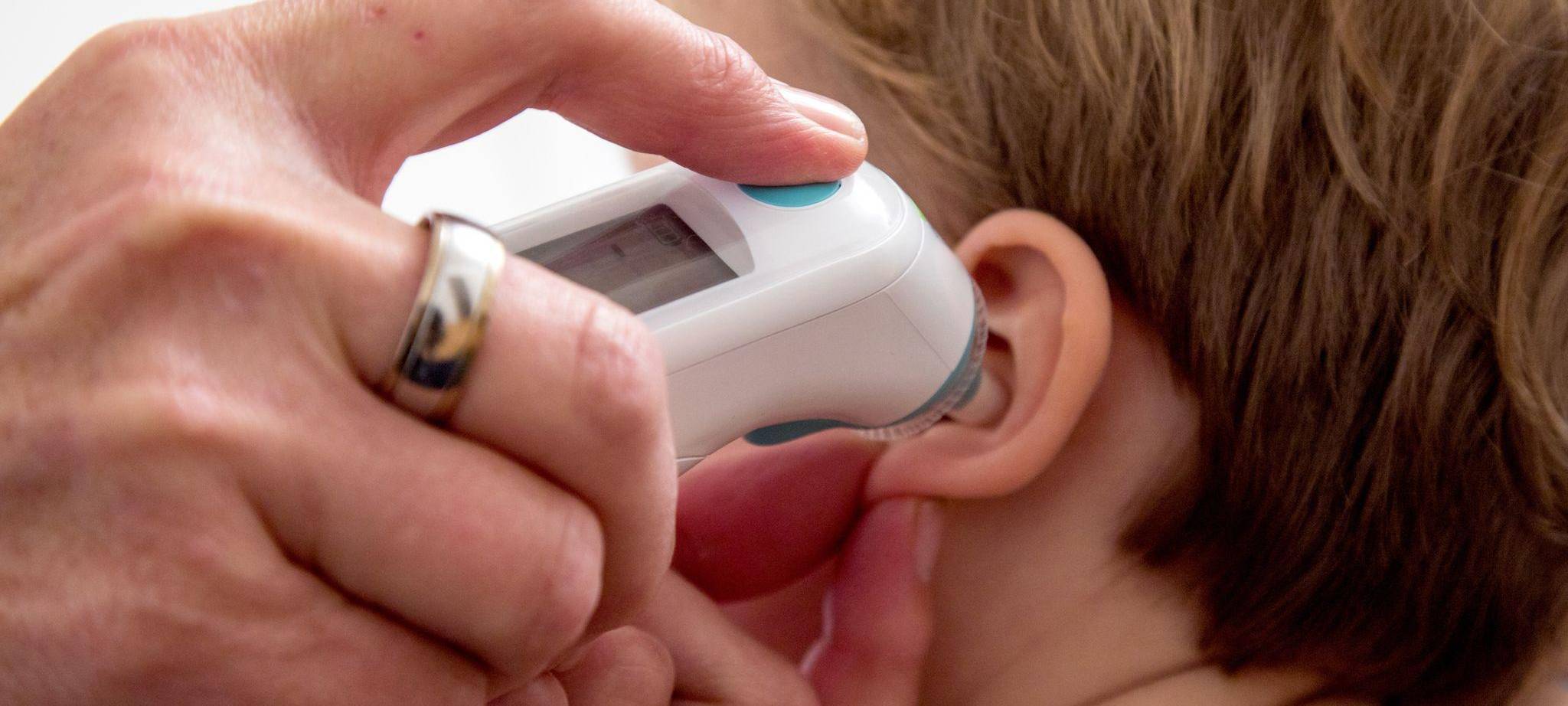 Eine Frau mißt bei einem Kind Fieber im Ohr
