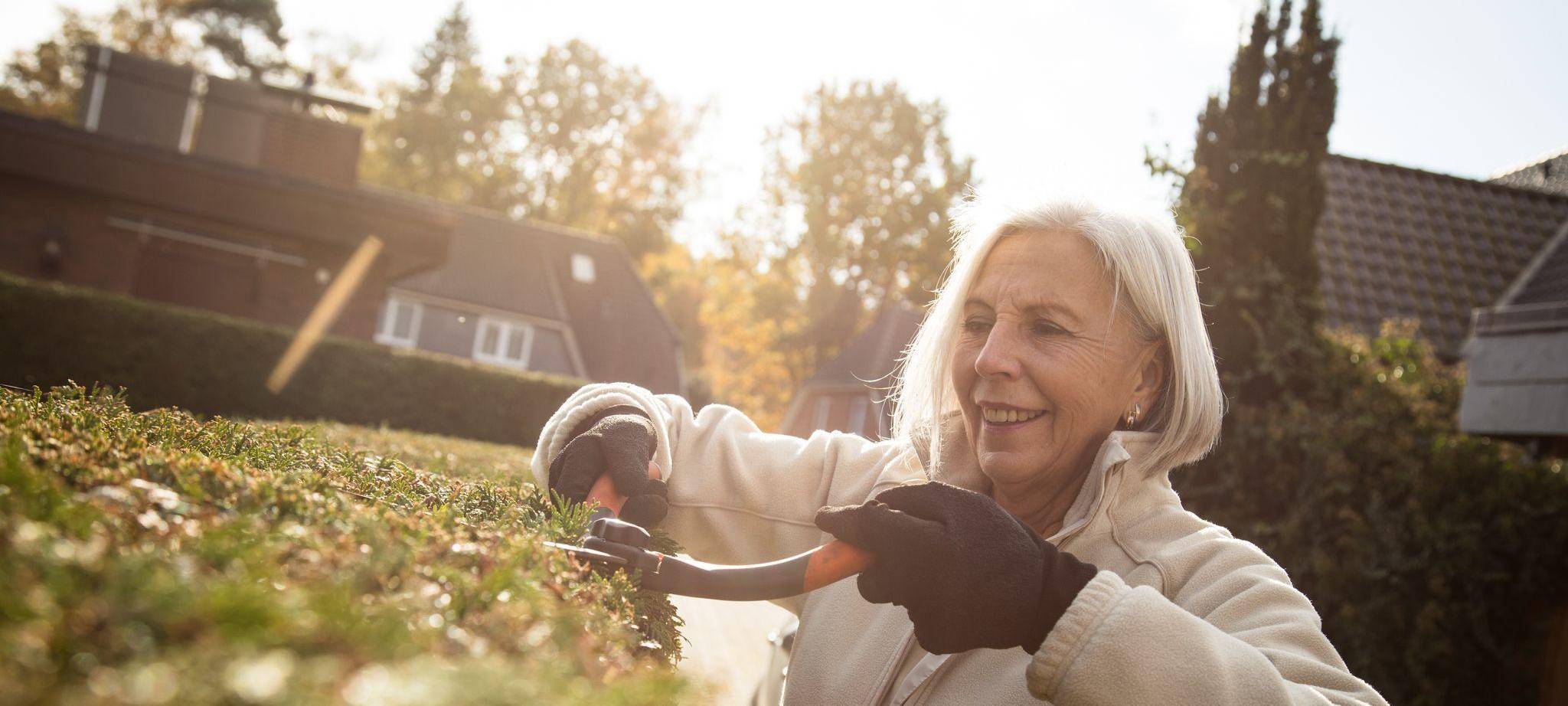 Eine ältere Dame schneidet eine Hecke