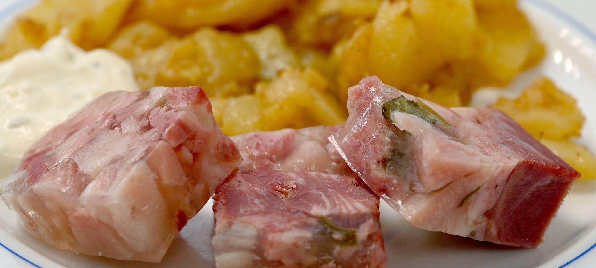 Sülze liegt auf einem Teller mit Bratkartoffeln