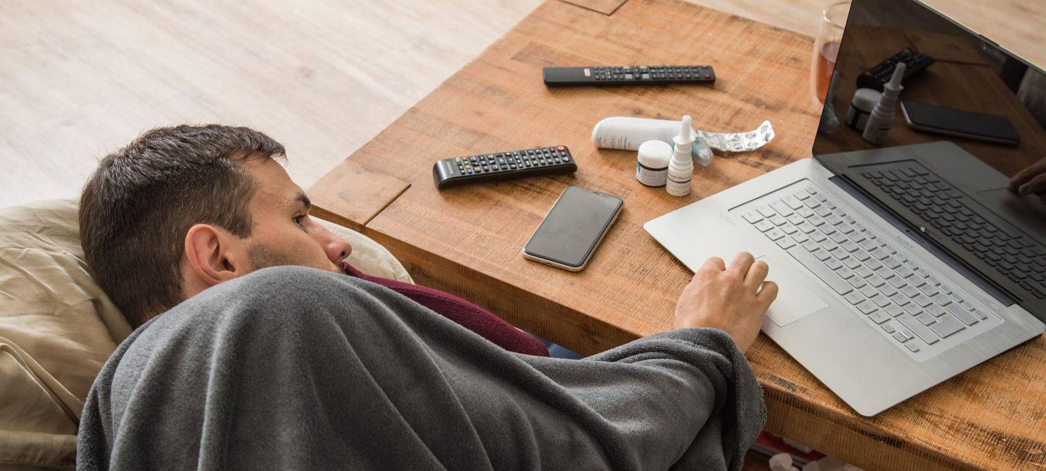 Ein Mann mit Erkltung bedient ein Laptop