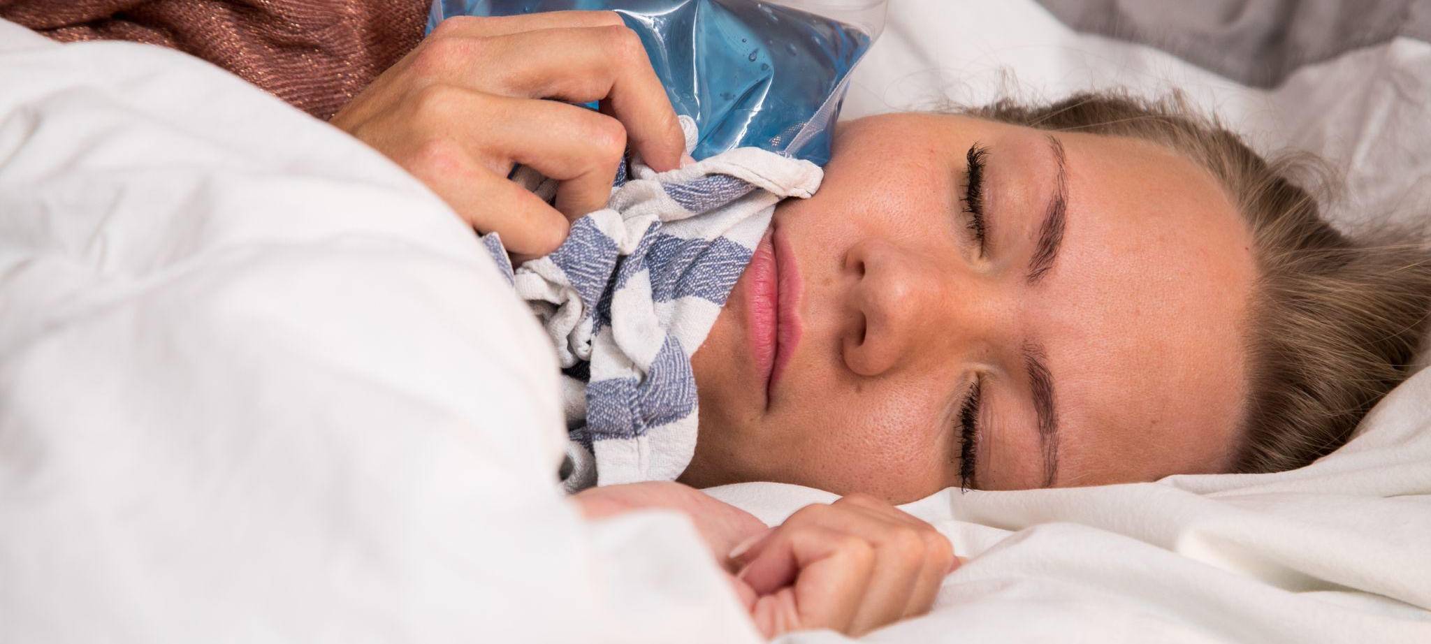 Eine Frau hält sich im Bett einen Kühlakku an die Wange