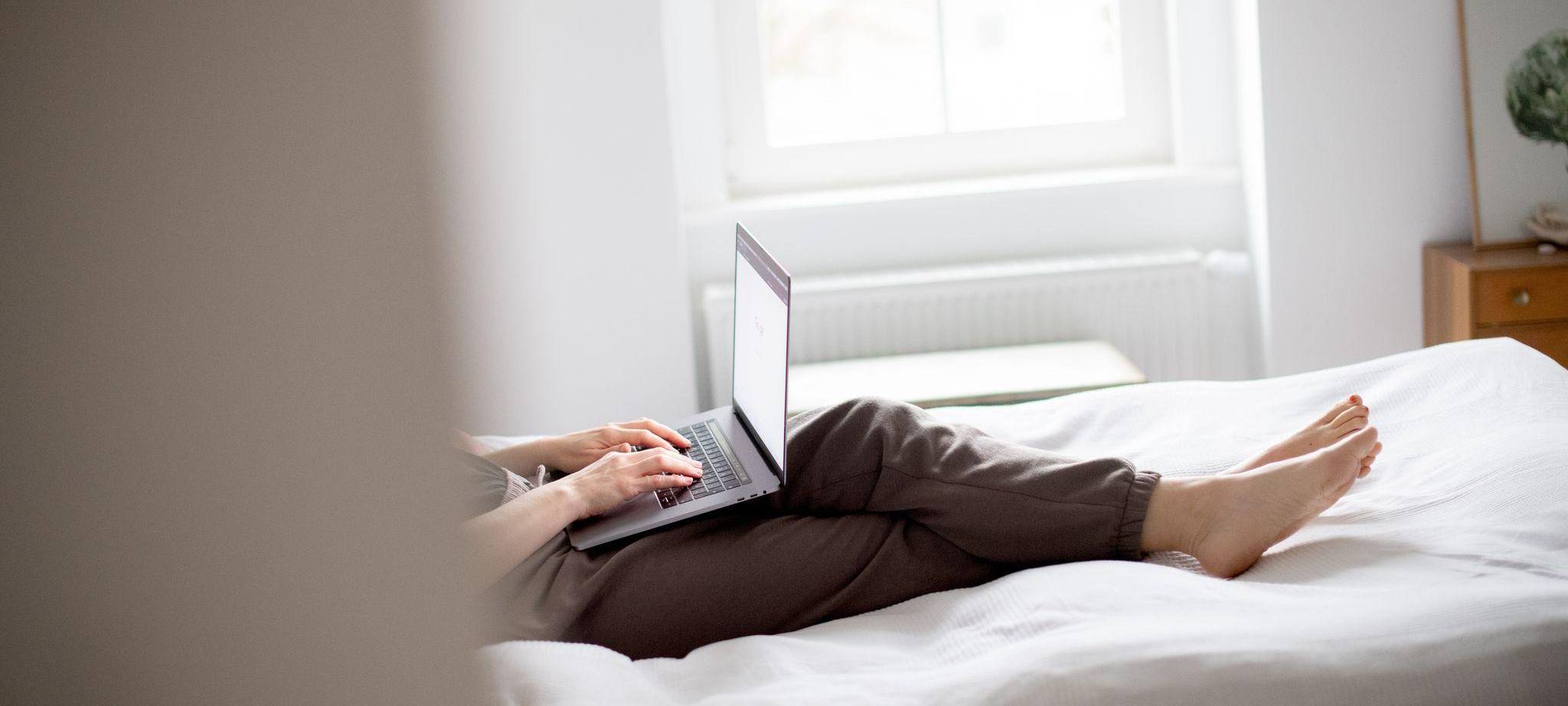 Eine Frau sitzt mit Laptop im Bett