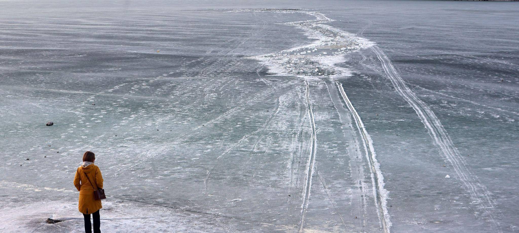 Eine Frau steht am zugefrorenem See nahe einer Einbruchstelle