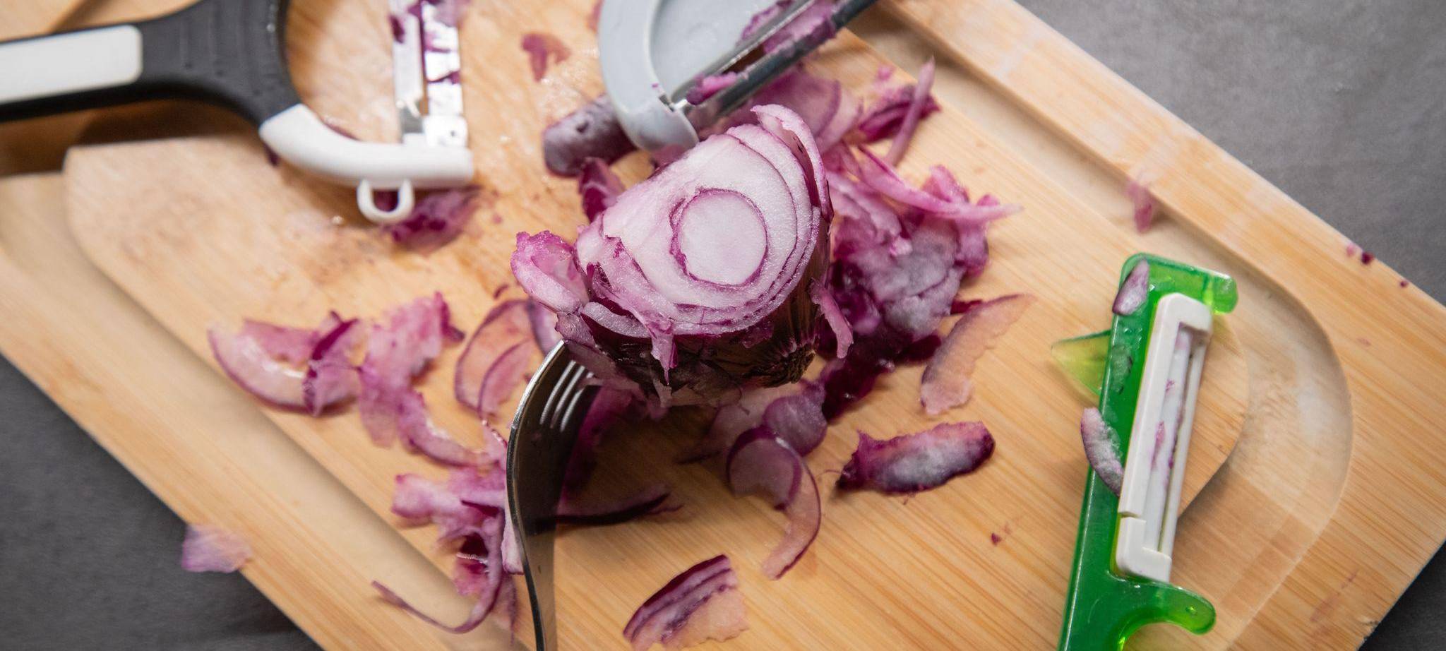 Verschiedene Sparschäler liegen neben einer Zwiebel